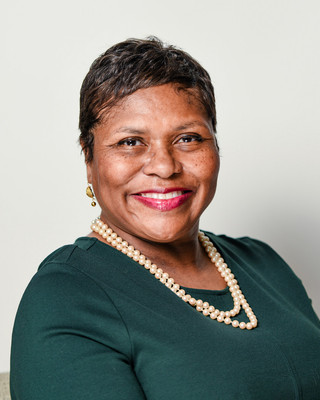 Professional headshot of a confident, middle-aged African American attorney in Baltimore, Maryland, wearing a pearl necklace and a green dress.